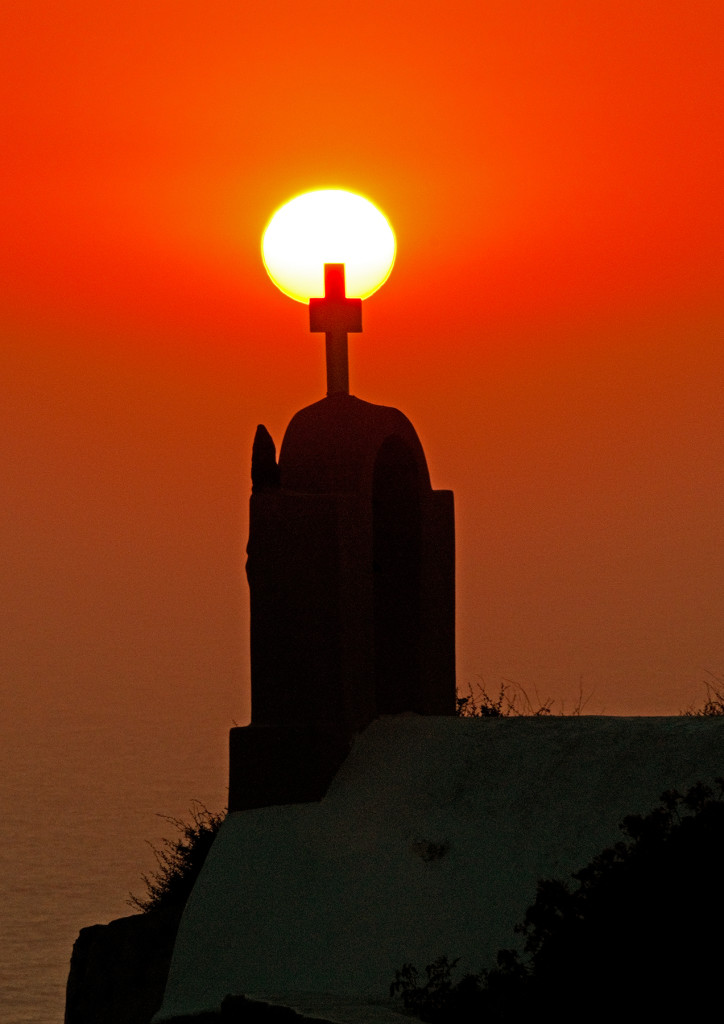 Sunset with silhouette of church cross in foreground, Oia, Santorini, Greece