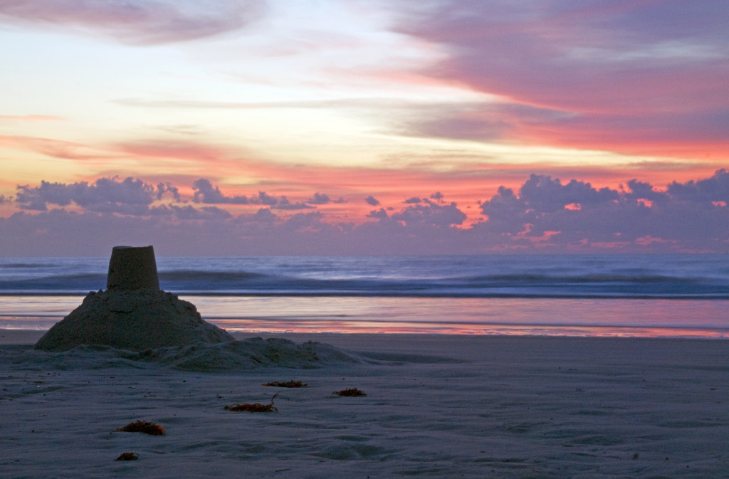 Sunrise at Cocoa Beach, Florida, with a sandcastle in the foreground and a dramatic sky